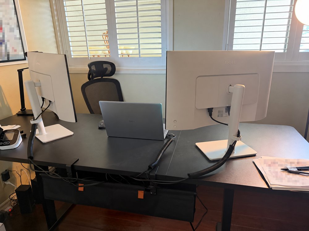 Rear view of two monitors with cable sleeves and cable routing beneath the desk